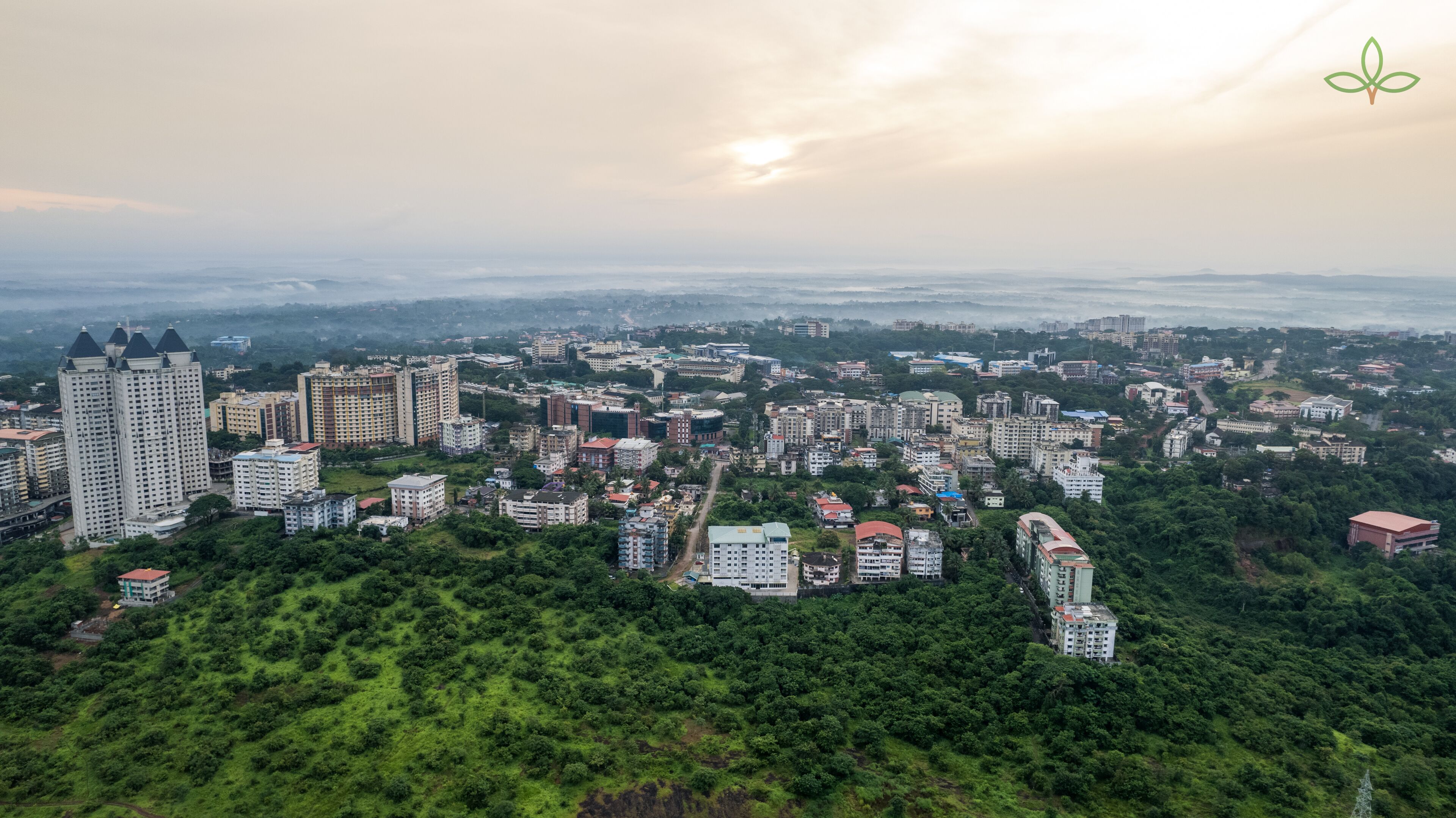 A cityscape with high-rise buildings, dense greenery, and a clear sky.