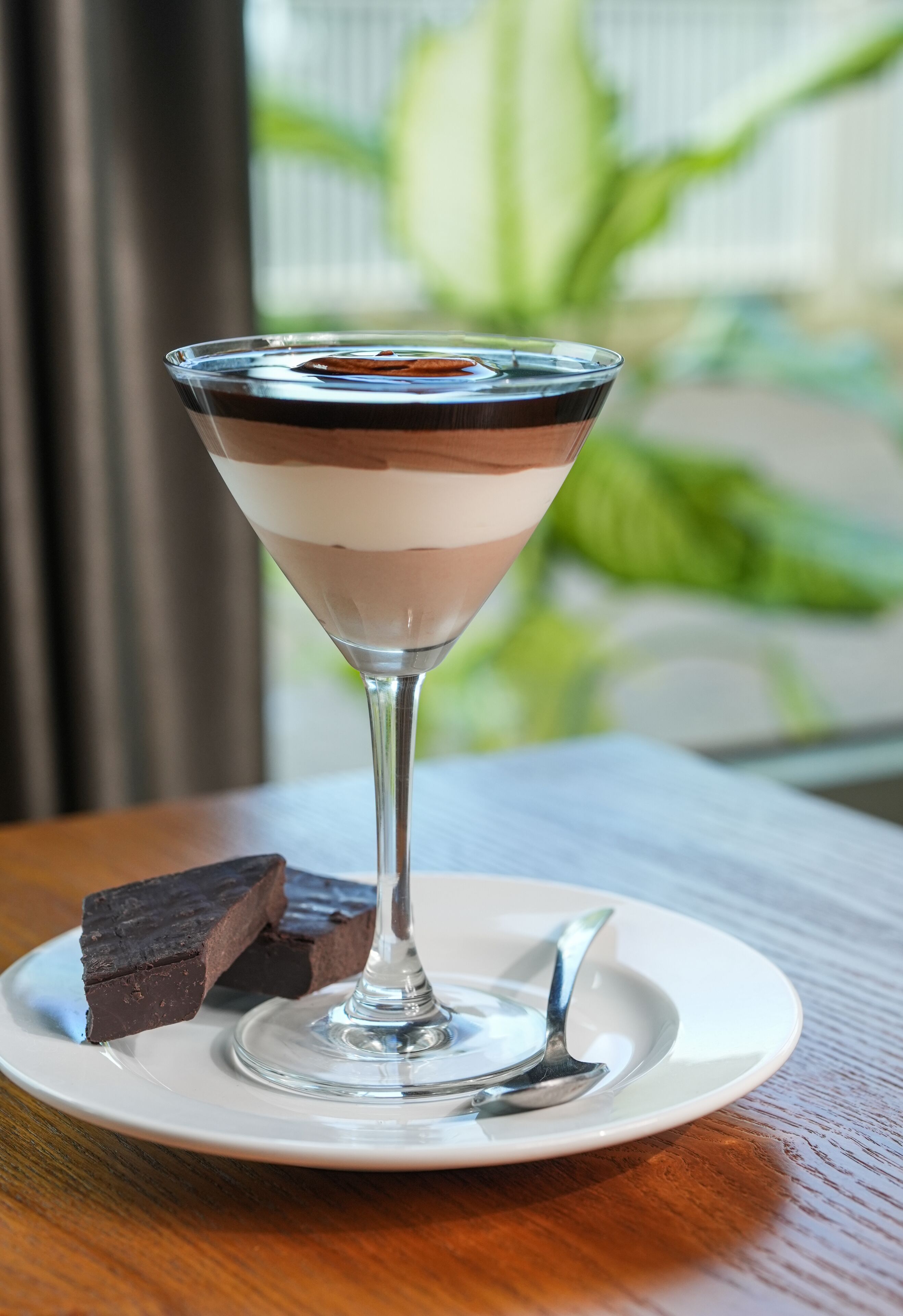 A dessert in a martini glass on a white plate with a fork beside it.