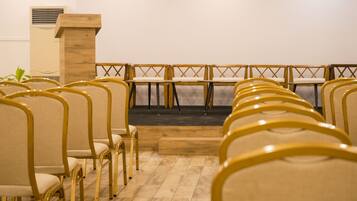 A row of yellow chairs with wooden frames and beige cushions, arranged in a semi-circular pattern facing a stage with a wooden podium.