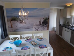 A dining area with a beach mural, white chairs, and a chandelier.