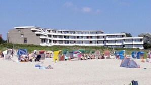 Un hotel sulla spiaggia con diversi balconi e una spiaggia sabbiosa in primo piano.