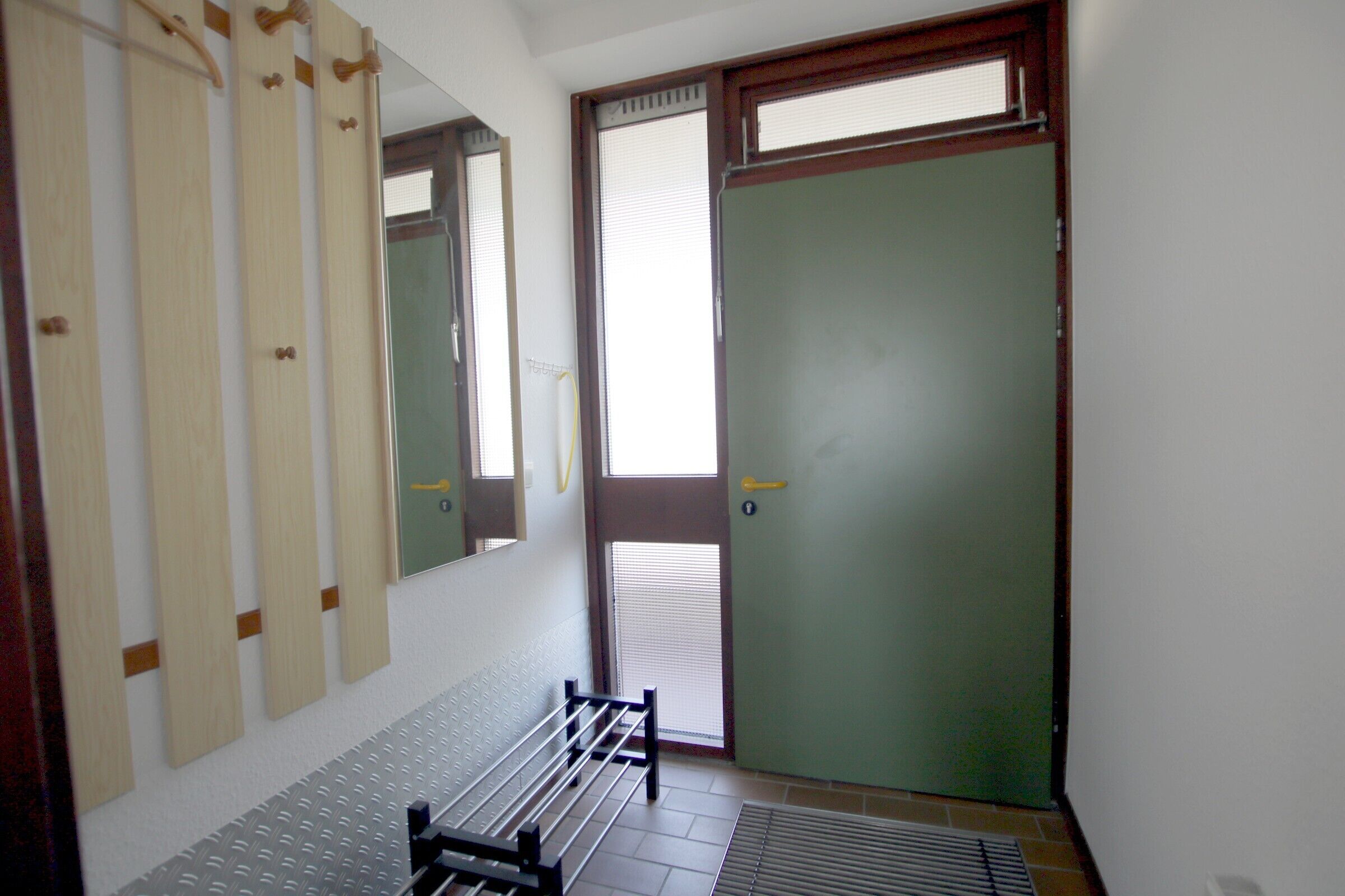 Una habitación con un banco, un espejo, una puerta y una ventana.
