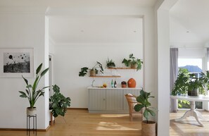Une cuisine lumineuse et spacieuse, avec des meubles en bois, un coin repas doté d’une table blanche et diverses plantes en pot.