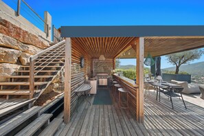 Un terrazzo in legno con area barbecue, posti a sedere all'aperto e una scala che conduce a un piano superiore.
