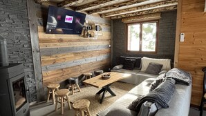 A cozy living room with a stone wall, wooden beams, a fireplace, a sofa, a coffee table, and a TV mounted on the wall.