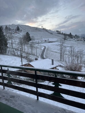 A snow-covered landscape with a winding road, a wooden fence, and a few buildings in the distance. - Chalet Les Sapins (La Bresse)