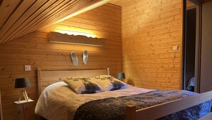 A cozy wooden cabin bedroom with a bed, two lamps, and a ceiling light.