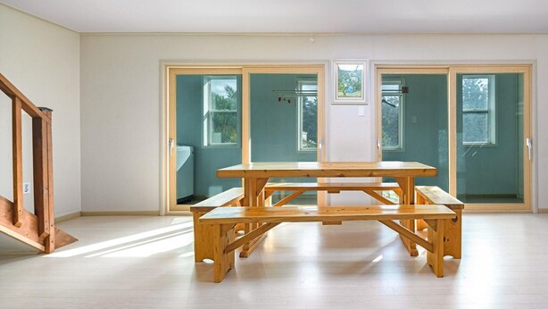 Amplia habitación con una mesa de madera y bancos, grandes puertas correderas de vidrio y una escalera.