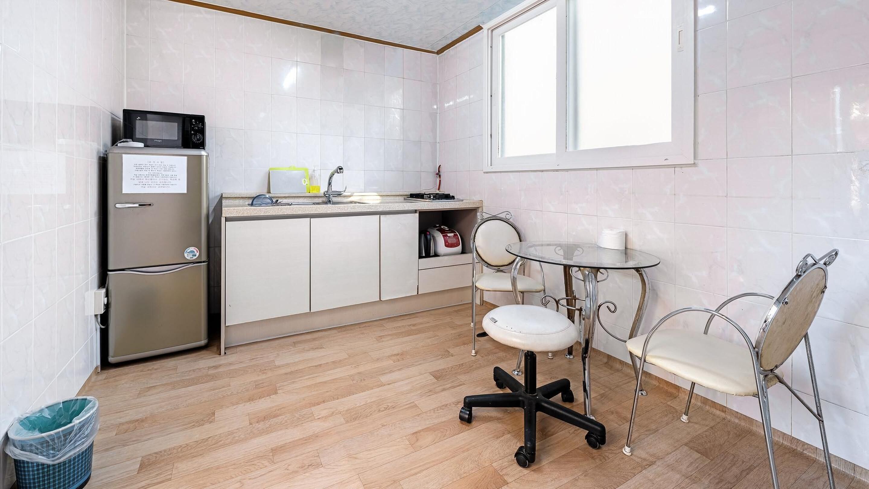 Une cuisine compacte équipée d’un réfrigérateur, d’un four à micro-ondes et d’un évier. On y trouve une petite table à manger avec des chaises, ainsi qu’une fenêtre qui laisse entrer la lumière naturelle.