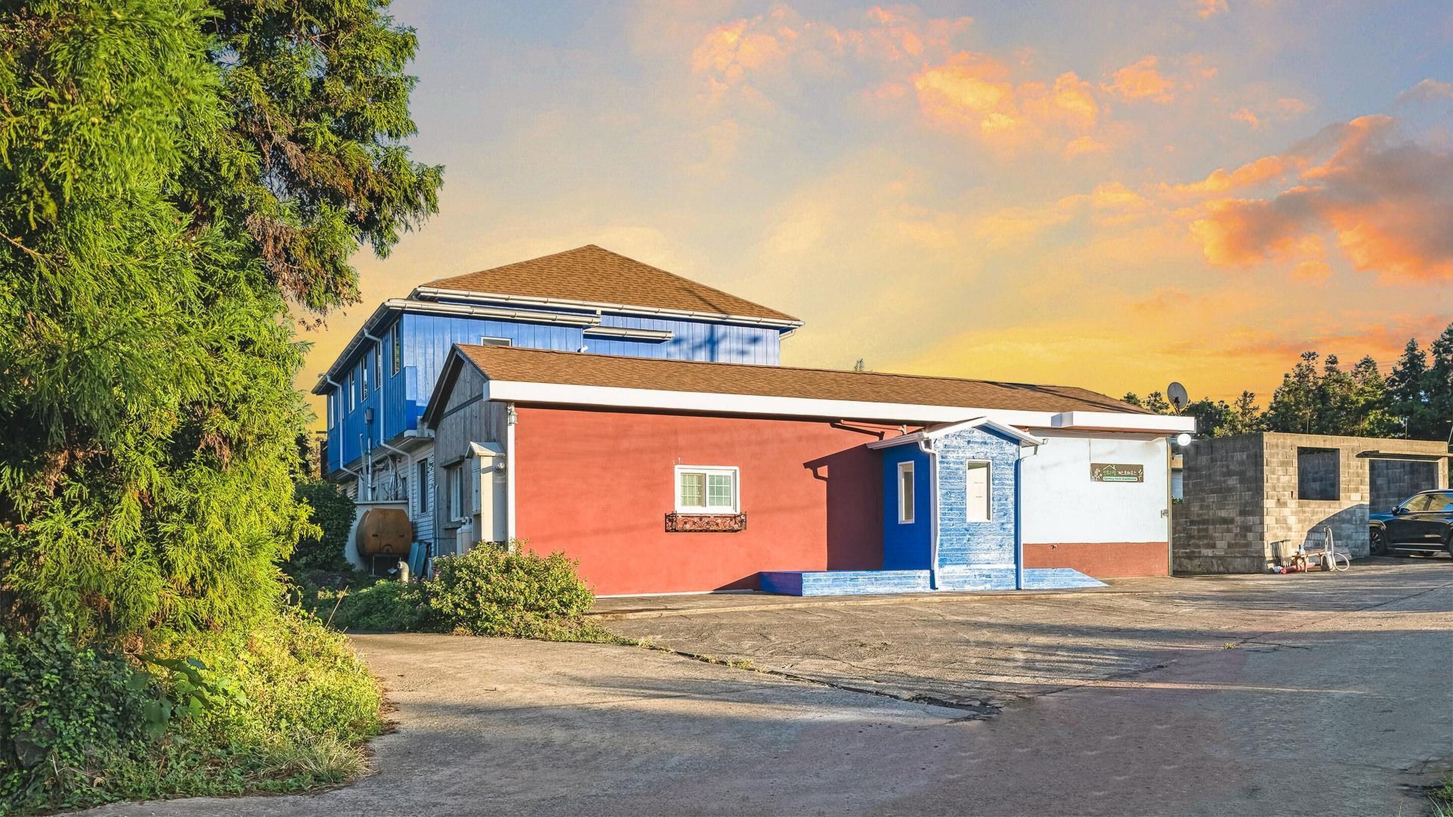 A two-story building with a red and blue facade, a small attached structure, and a parking area.