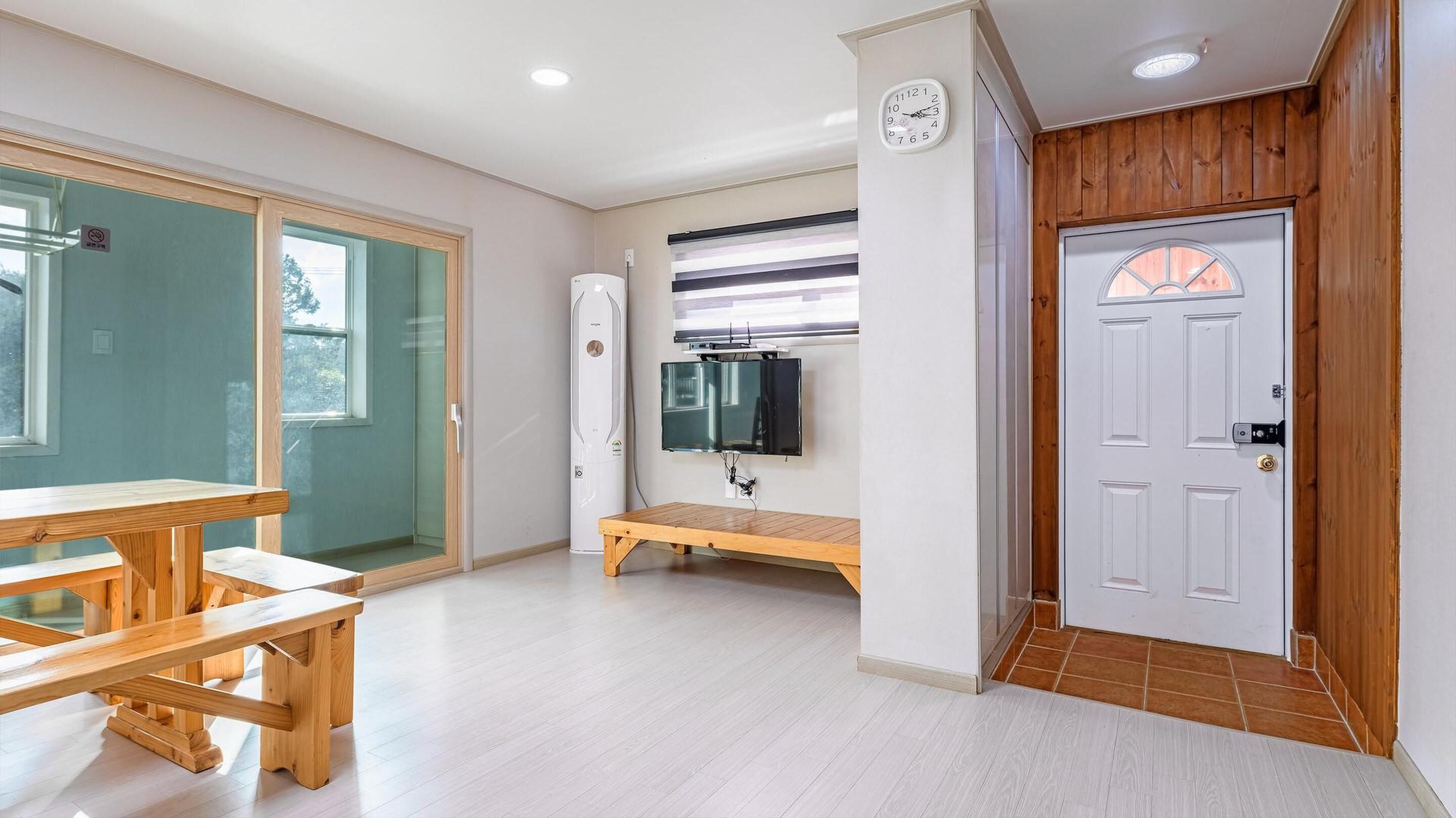 Een moderne kamer met een houten bank, een aan de muur bevestigde televisie en een witte deur met raam.
