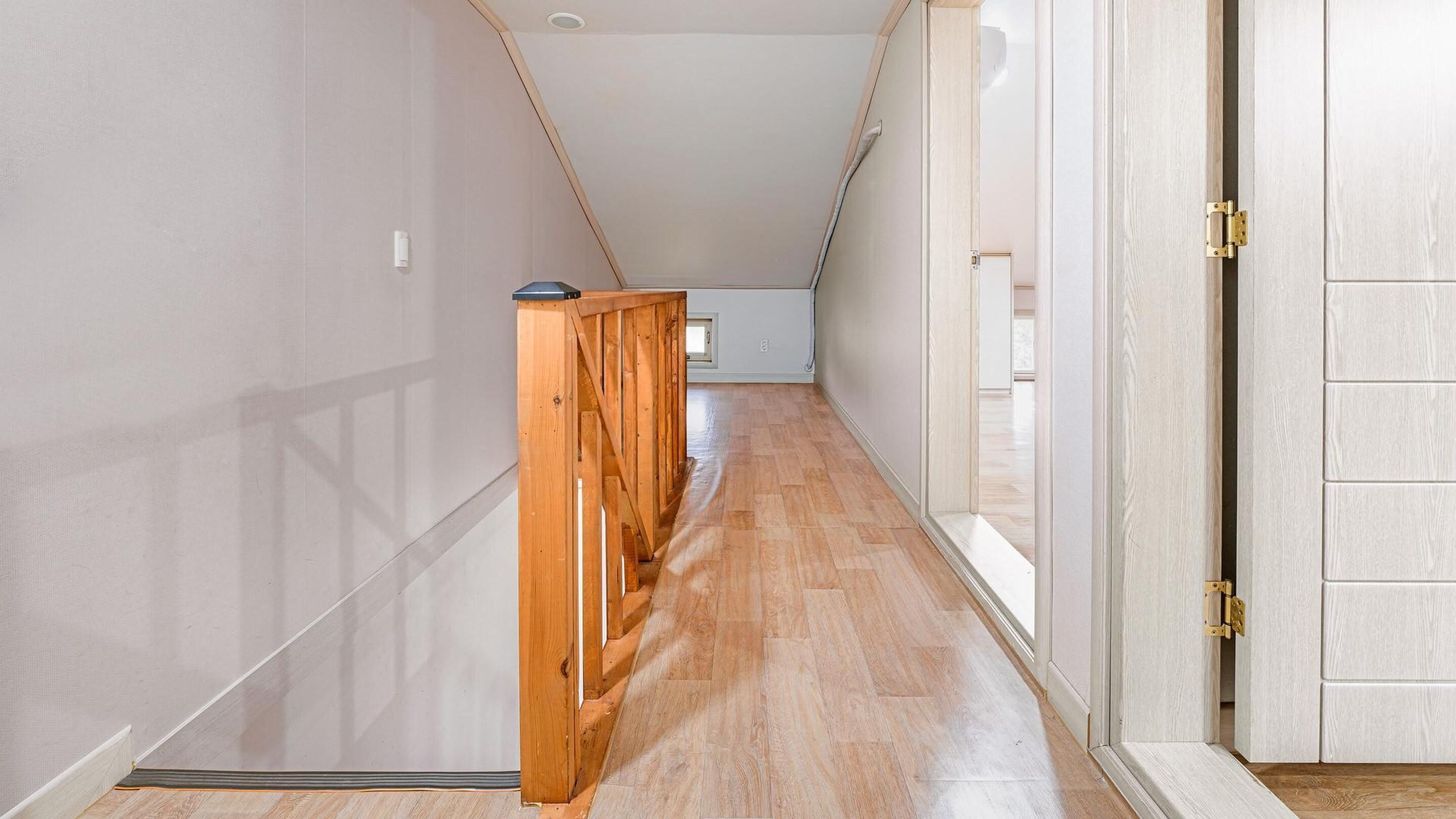 A narrow hallway with wooden flooring and a wooden railing.