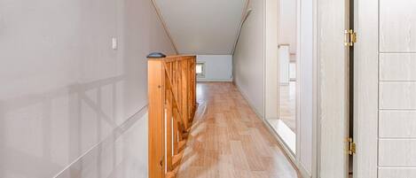 A narrow hallway with wooden flooring and a wooden railing.