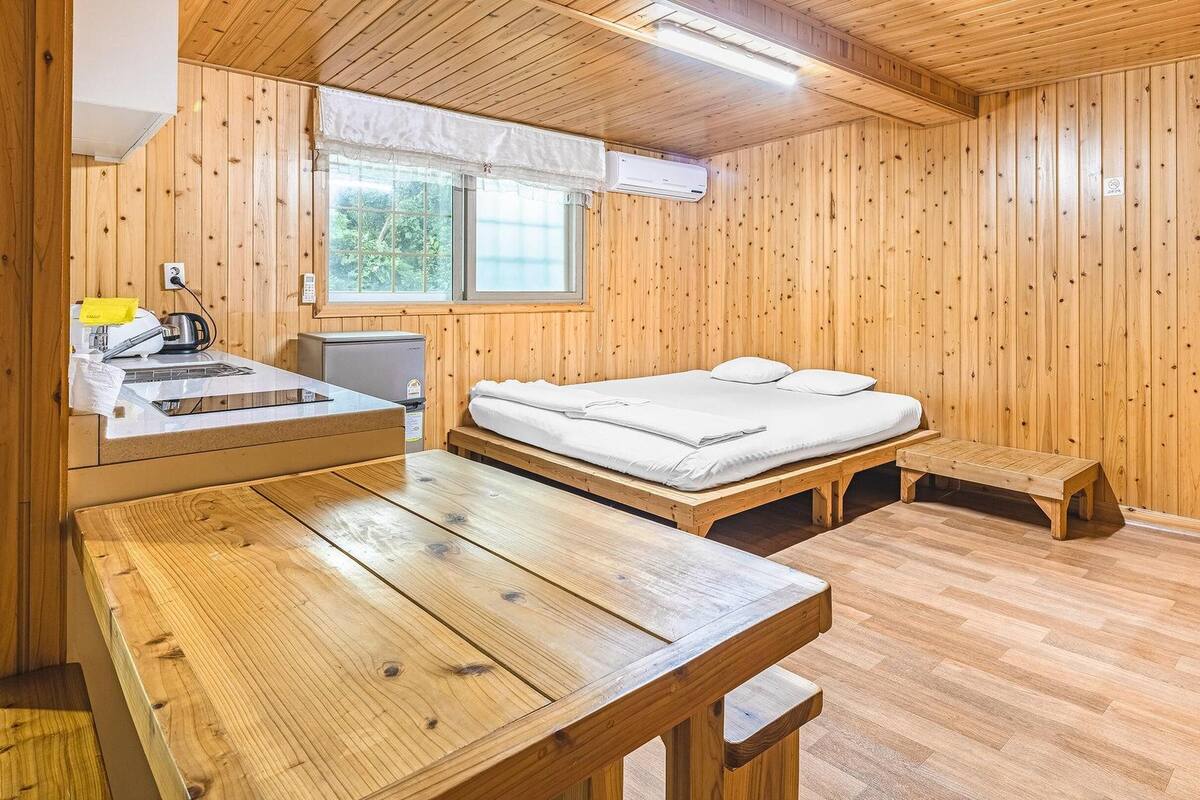 A wooden cabin room with a bed, a small table, and a window.
