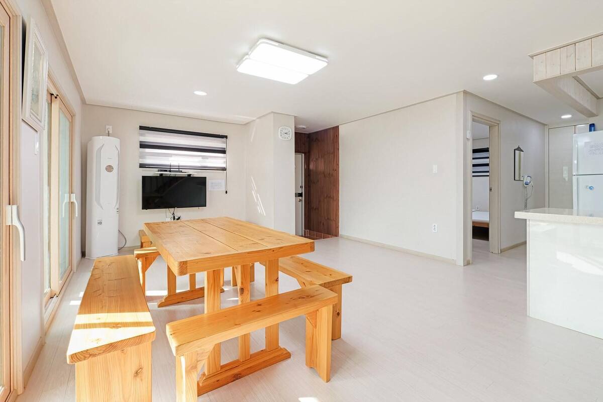 A modern kitchen with a wooden dining table and benches, a built-in fridge, and a TV mounted on the wall.
