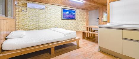 Una habitación pequeña con cama, un banco de madera, una mesita y un rincón americano.