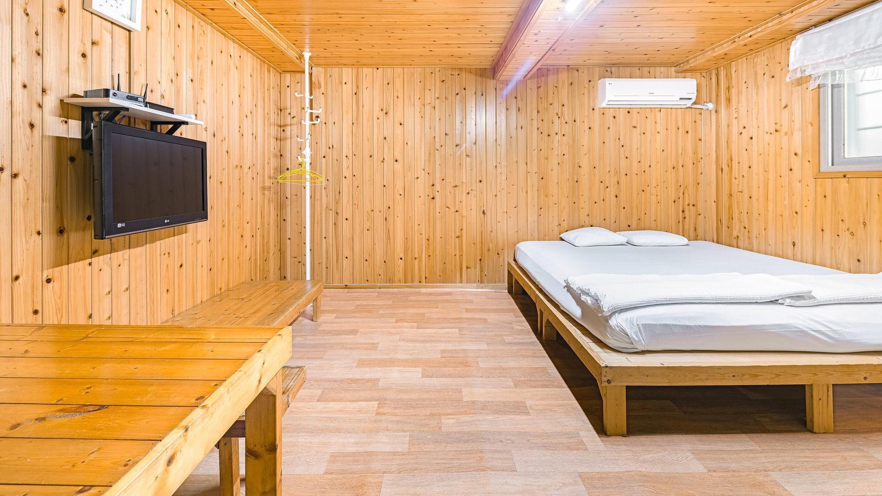 A wooden-paneled room with a bed, a TV, and a bench.