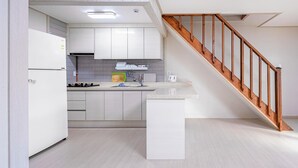 Una cocina moderna con armarios blancos, horno empotrado y escalera de madera.
