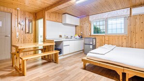 Una cabaña de madera con cocina, una mesa de comedor y una cama.