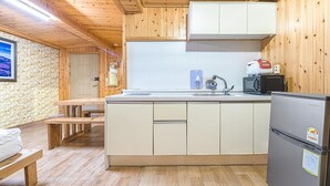 Cocina compacta con armarios de madera, un lavamanos integrado, un refrigerador y una zona de comedor con un banco.