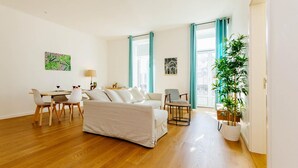 Un salón espacioso con sofá, mesa de comedor, sillas y un amplio ventanal con cortinas.