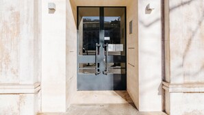 Una entrada moderna con puerta de cristal, reja metálica y un pequeño letrero en la pared.