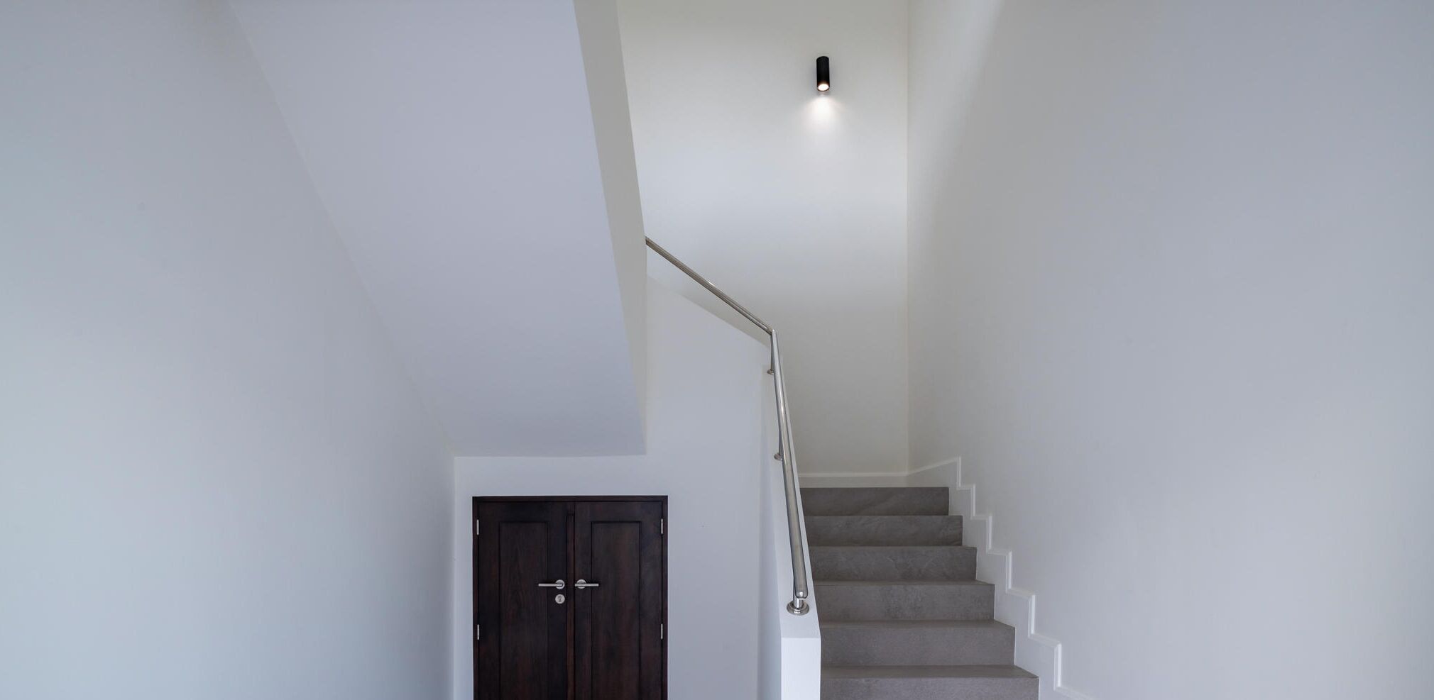 A staircase with a handrail, a door, and a light fixture on the wall.