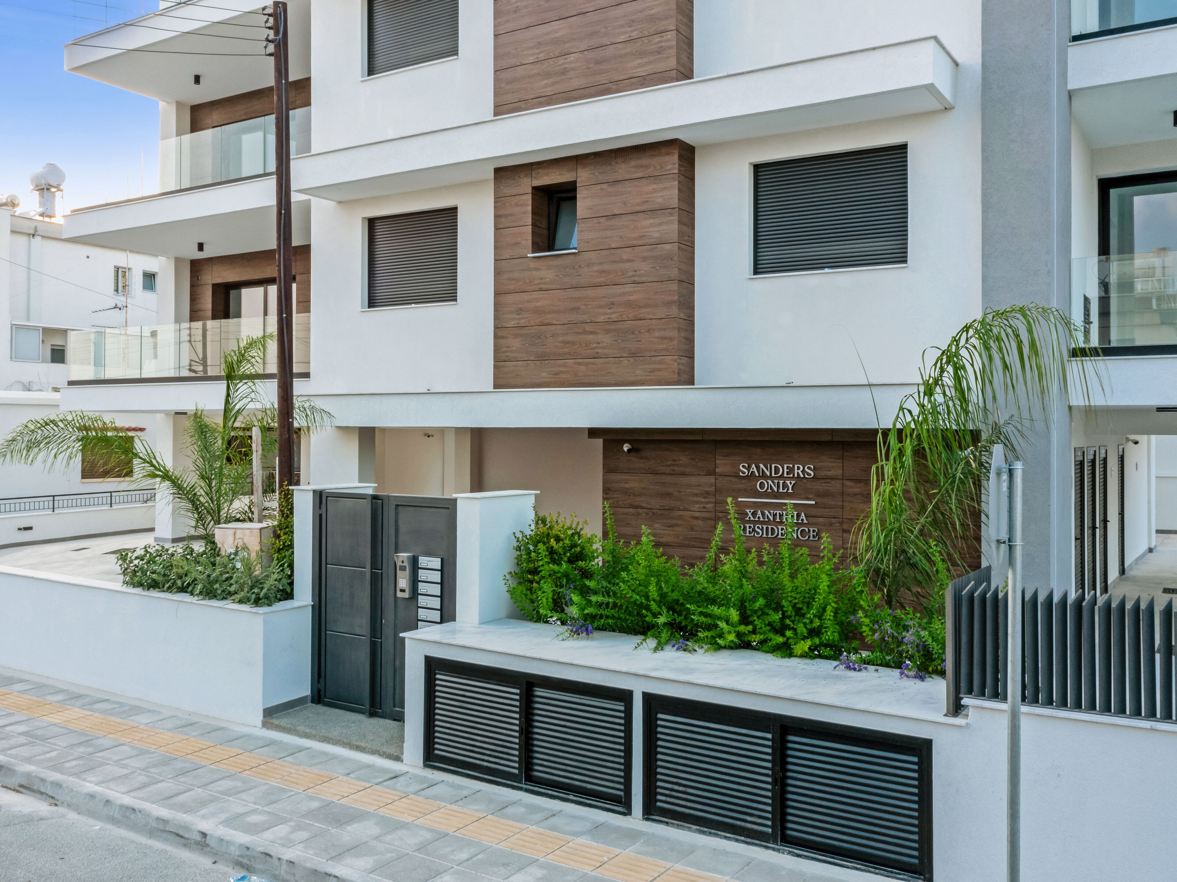 A modern apartment building with a gated entrance, a sign indicating 'SANDERS ONLY XANTHA RESIDENCE', and a well-maintained garden area.