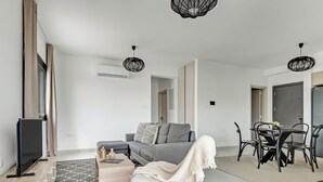 A modern living room with a grey sofa, a TV, and a dining area with a table and chairs.