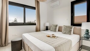 A modern hotel room with a large bed, two bedside tables, a window with a view, and a hanging light fixture.