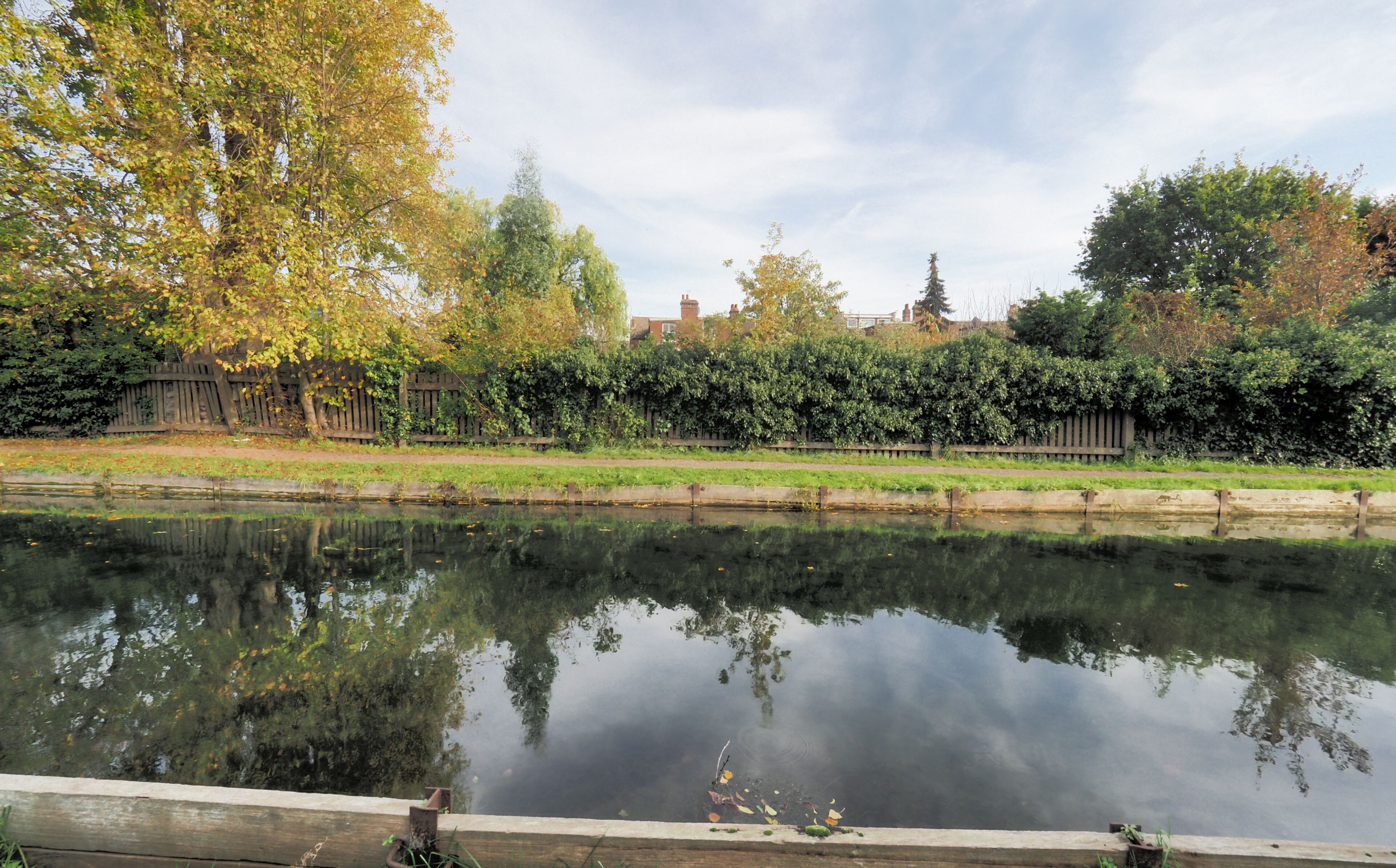 A calm river reflecting trees and a wooden fence.