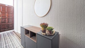 Un couloir avec une porte en bois, une console grise ornée de plantes et un mur à motifs.