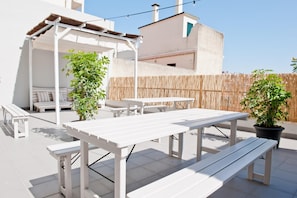 An outdoor patio with white furniture, including tables and benches, surrounded by a bamboo fence.