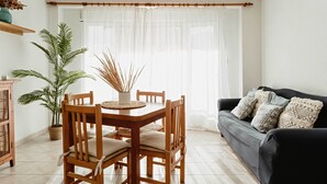 Un comedor con mesa y sillas de madera, una planta en maceta y un sofá con cojines.