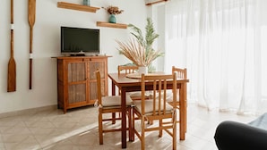 Un comedor con una mesa y sillas de madera, un televisor sobre un mueble de madera, y una planta en un estante.
