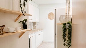 Una cocina moderna con armarios blancos, un estante de madera, una olla negra con una planta y un colgador de macramé para plantas.