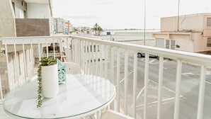 Un balcón con una mesa de vidrio, una planta en maceta y vistas a un estacionamiento y edificios.