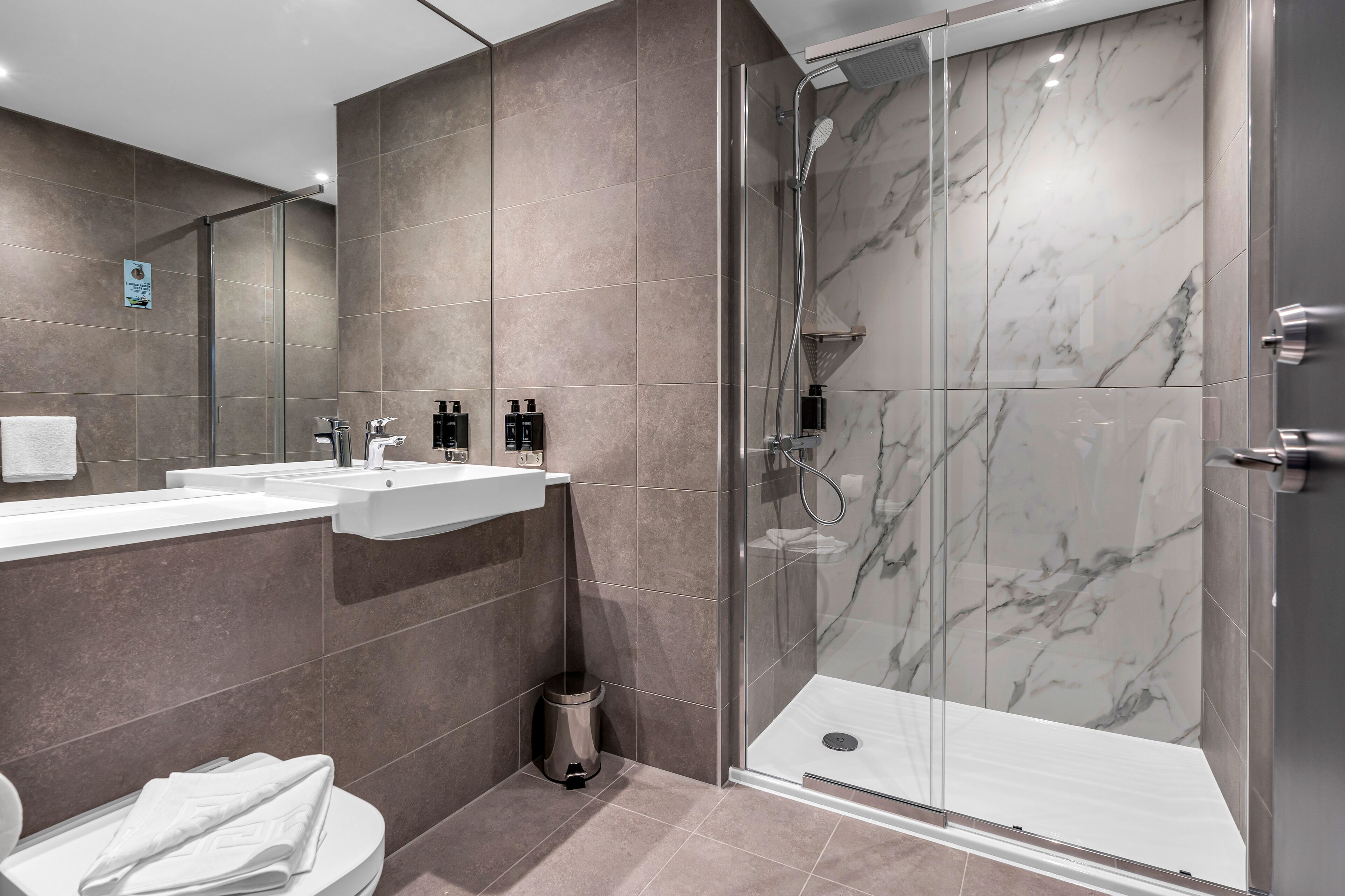 A modern bathroom with a glass-enclosed shower, two sinks, and a toilet.