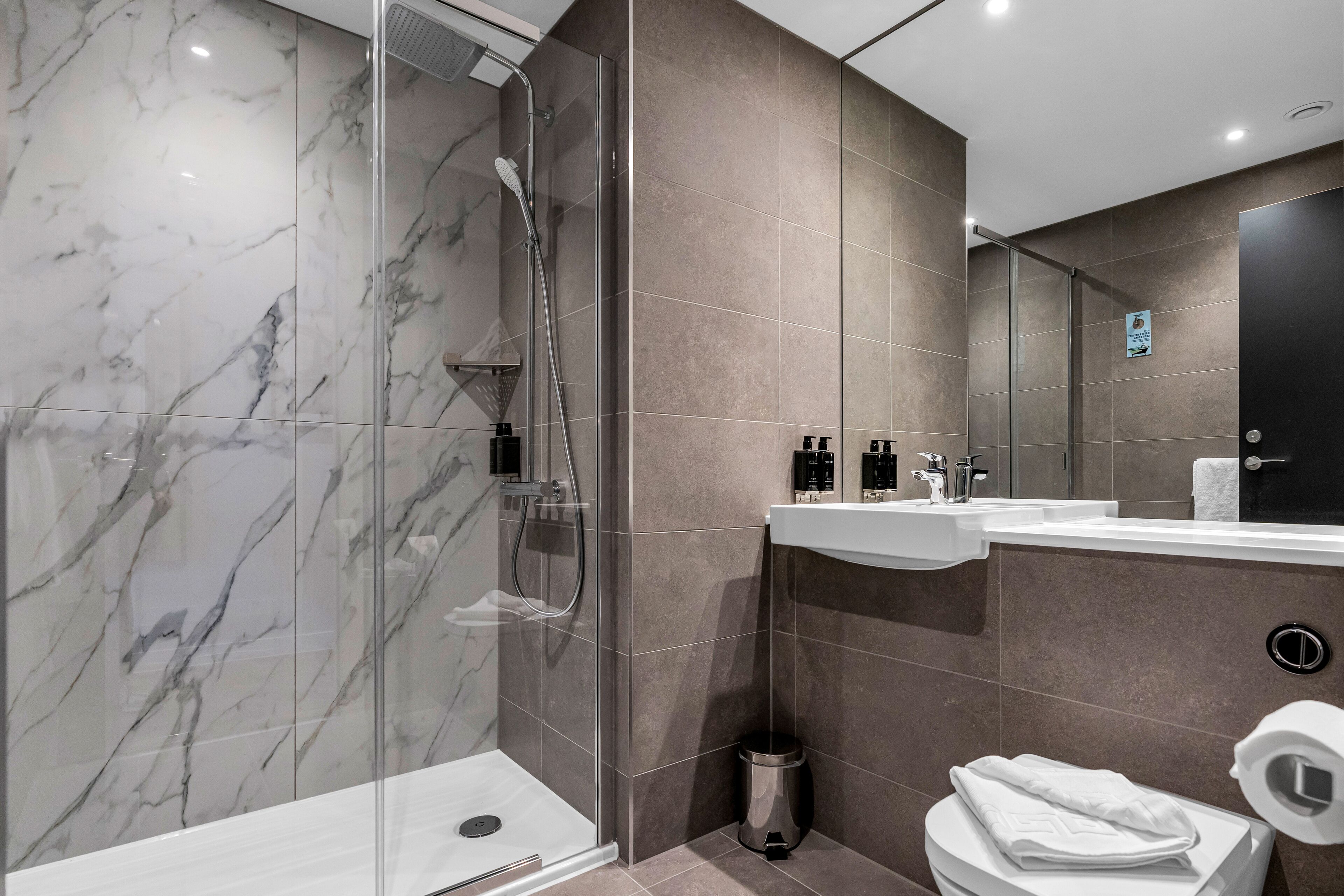 A modern bathroom with a glass-enclosed shower, a white sink, and a toilet.