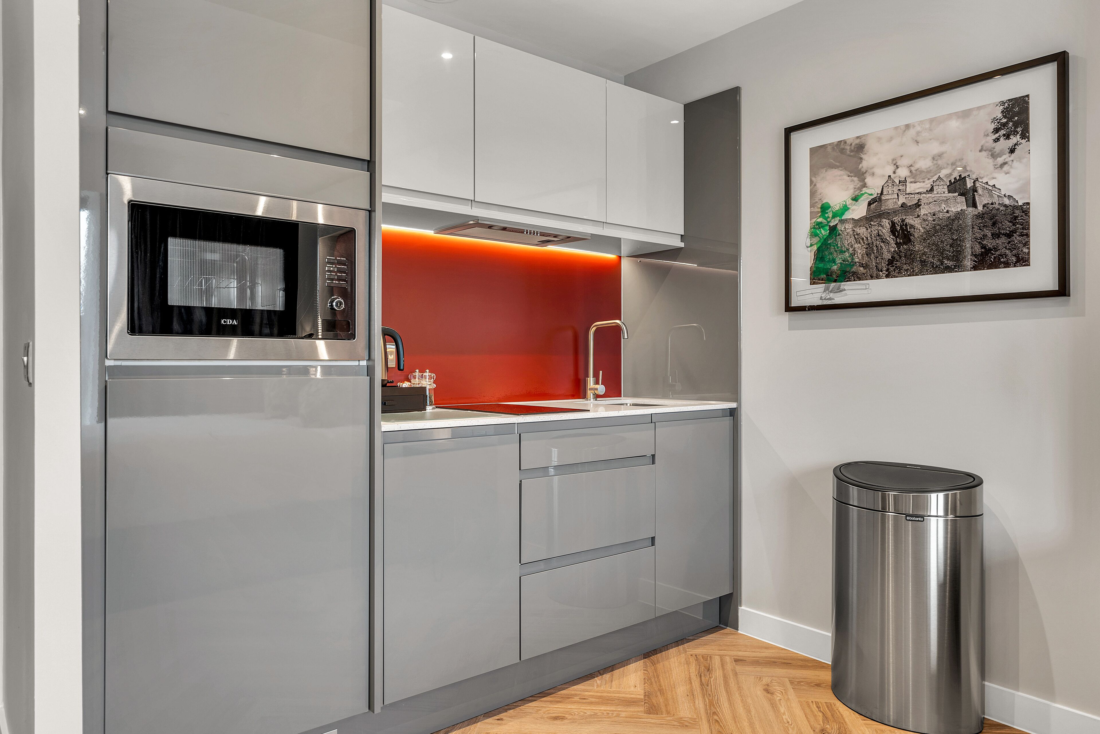 A modern kitchen with stainless steel appliances, a red accent wall, and a framed picture on the wall.