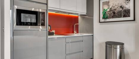 A modern kitchen with stainless steel appliances, a red accent wall, and a framed picture on the wall.