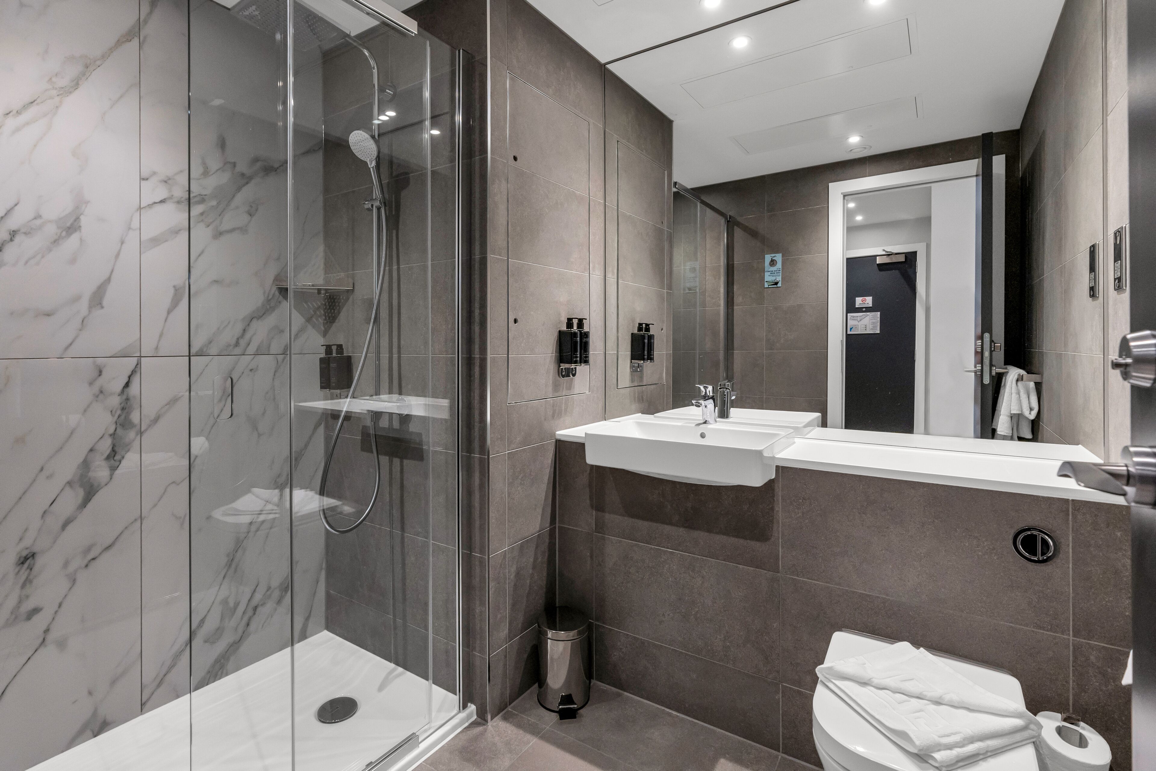 A modern bathroom with a glass-enclosed shower, two sinks, and a toilet.