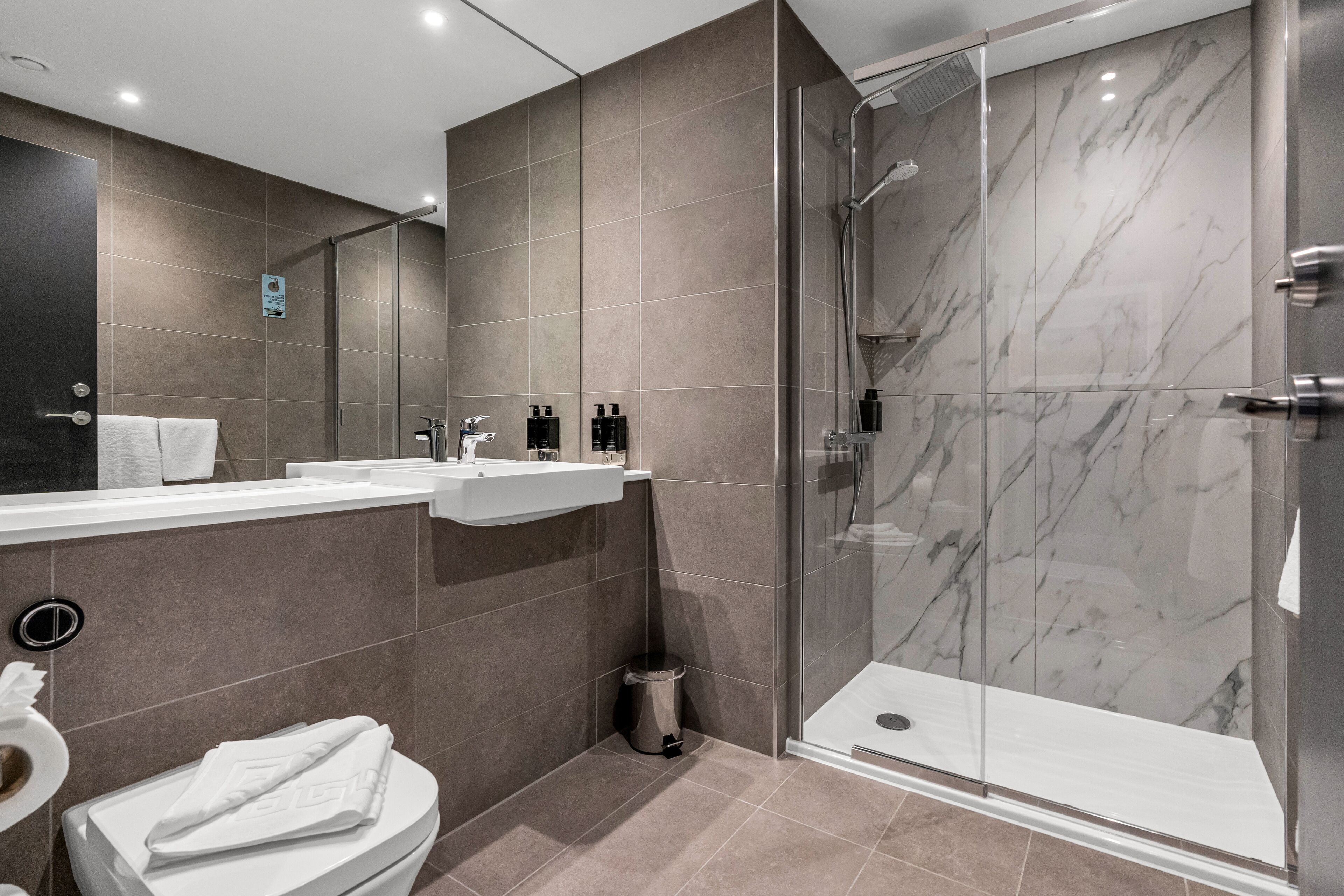 Un baño moderno con ducha envuelta en vidrio, lavamanos blanco y retrete.