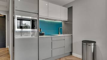 A modern kitchen with a stainless steel refrigerator, a blue backsplash, and a trash can.