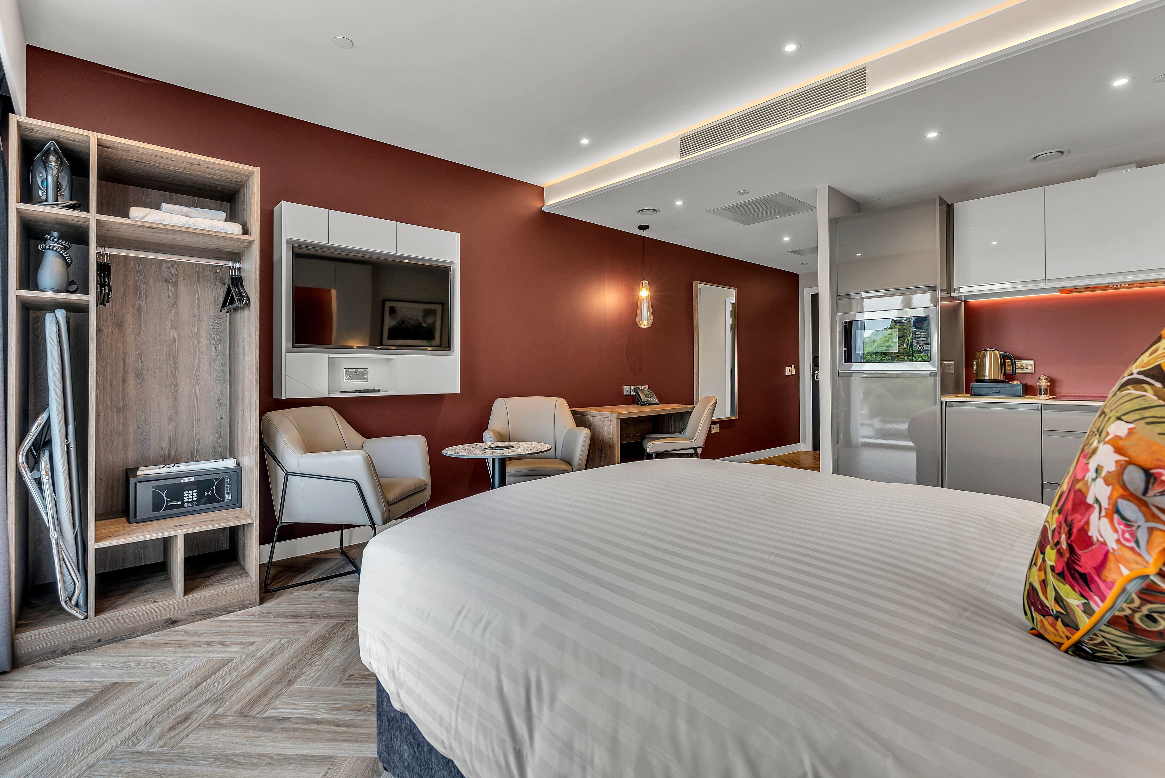 Et moderne hotelværelse med en stor seng, et siddeområde med stole, et lille bord, et fjernsyn og et tekøkken.