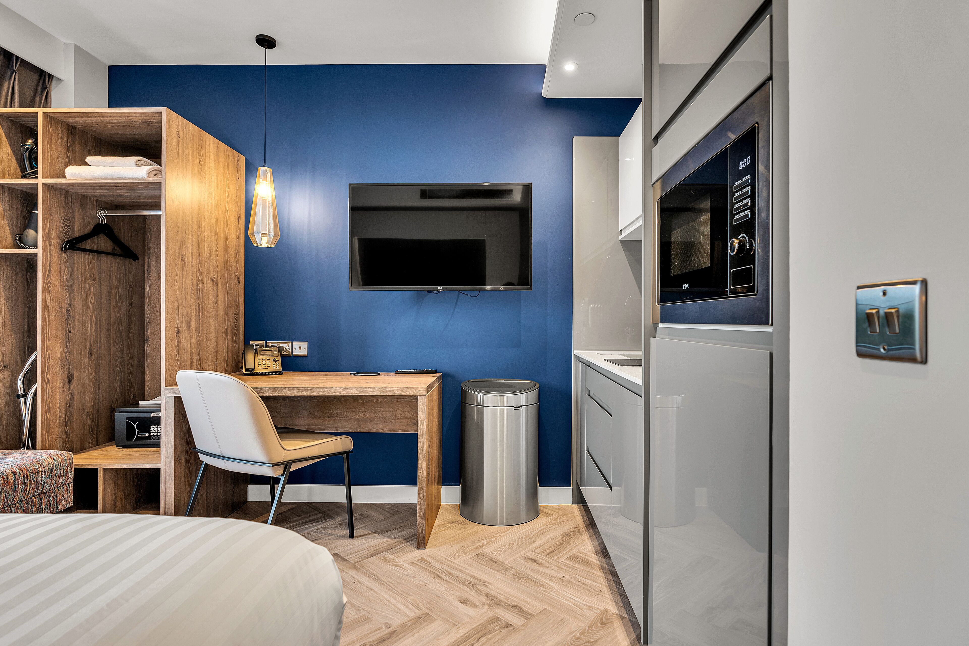 Een moderne hotelkamer met een houten bureau, een stoel, een bed, een aan de muur bevestigde televisie en een prullenbak.