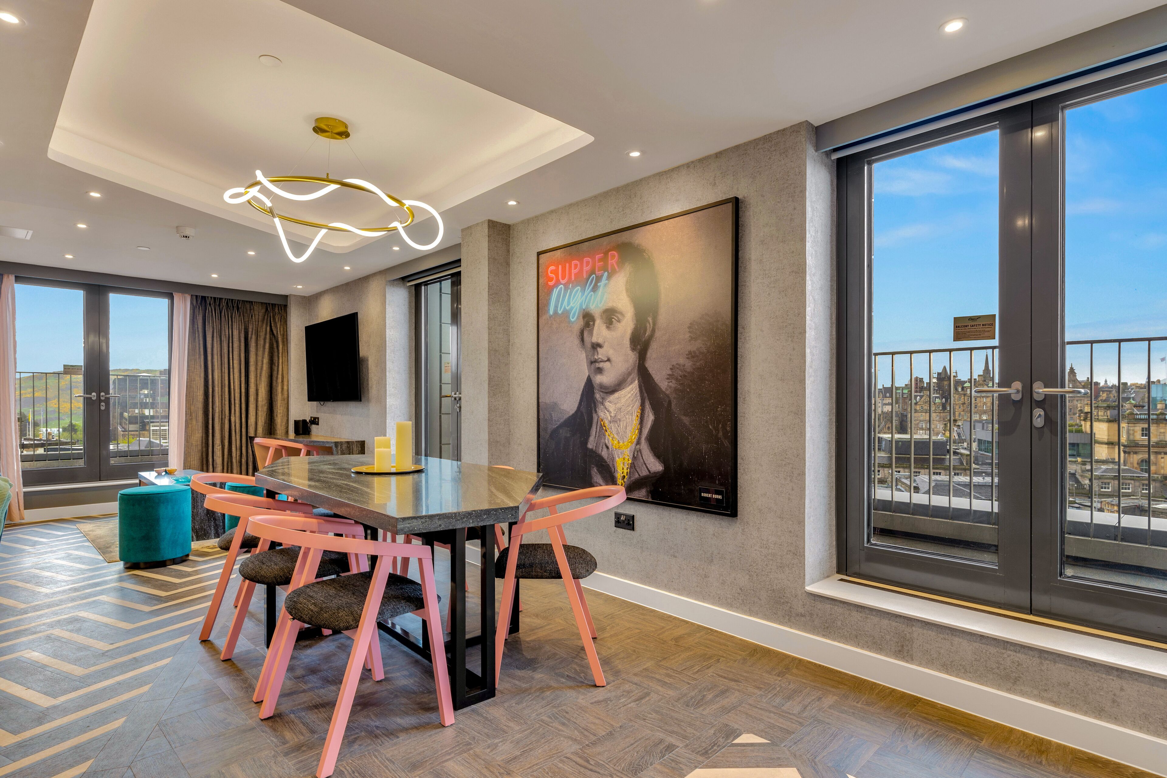 A modern dining area with a large table, pink chairs, and a city view through large windows.