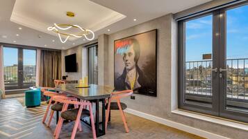 A modern dining area with a large table, pink chairs, and a city view through large windows.