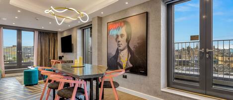 Un espace de salle à manger moderne, avec une grande table, des chaises roses et une vue sur la ville grâce à de grandes fenêtres.
