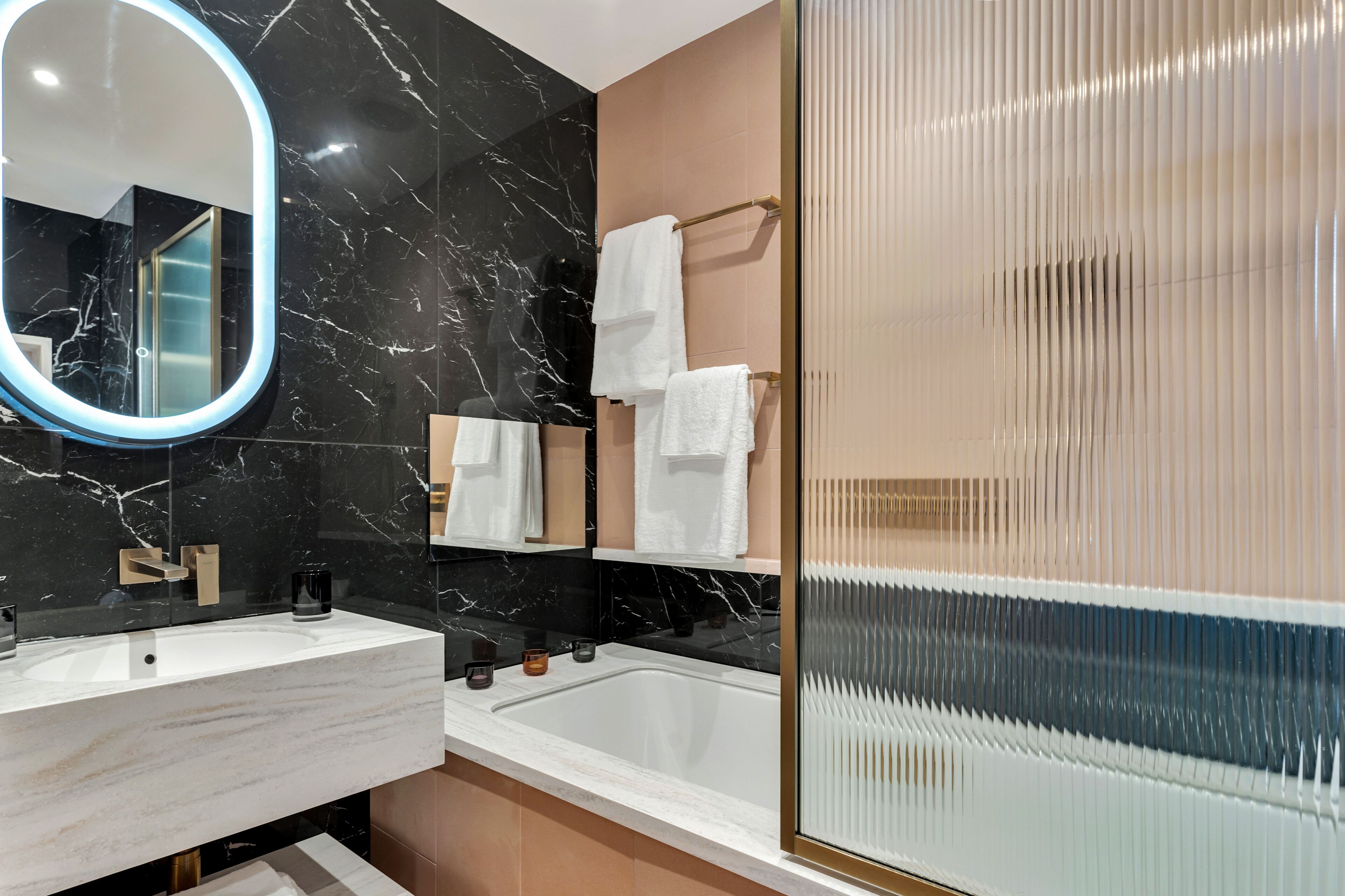 A modern bathroom with a marble vanity, a large mirror, a bathtub, and a shower with a frosted glass door.